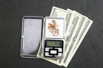 Gold jewelry on the scales and money on a black background