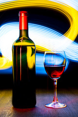 Bottle and a glass of wine on bright background with bokeh effect.