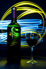 Bottle and a glass of wine on bright background with bokeh effect.