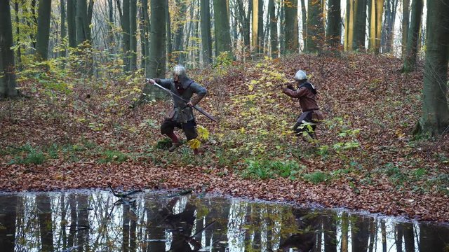 Medieval Vikings running through the forest reflected in water.