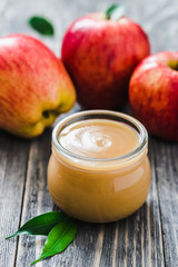 Applesauce in glass jar and red ripe apples on rustic wooden background. Selective focus, space for text. 
