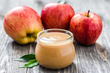 Slow cooker plum applesauce in glass jar and red ripe apples on rustic wooden background. Selective focus, space for text. 