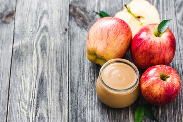 Healthy unsweetened applesauce in glass jar and red ripe apples on rustic wooden background. Selective focus, space for text. 