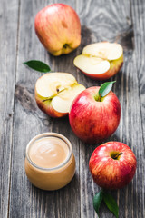 Homemade unsweetened applesauce in glass jar and red ripe apples on rustic wooden background.Top view, copy space.