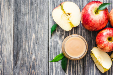 Crock pot applesauce in glass jar and red ripe apples on rustic wooden background. Top view, copy space.