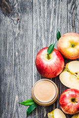 Healthy baby food, applesauce in glass jar and red ripe apples on rustic wooden background. Top view, copy space.