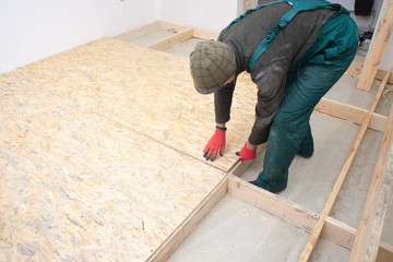 Man worker fits wooden oriented stands bords on insulated floor. New house constuction