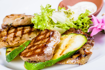Grilled meat and zucchini decorated with lettuce on white plate