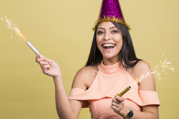 charming cheerful caucasian female wearing party hat holding sparkler fireworks , isolated on yellow studio background