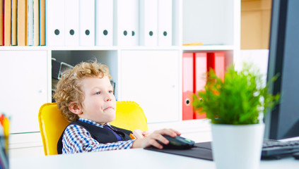 Short break at work. Curly Caucasian boy eats a sandwich with sausage in the workplace in the office looking at the computer screen