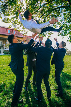 Wedding funny day. Groomsmen throw groom up standing in the park. 