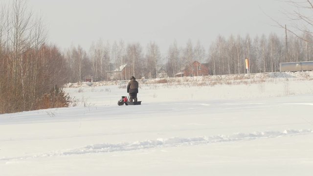 Man in winter clothes riding on mini snowmobile on deep snowdrifts in the field, walking with snow and waving his hands