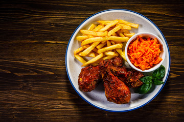 Barbecued drumstick with french fries and vegetable salad on wooden table 