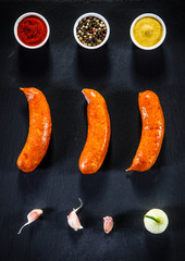 Sausages with spices on black stone on wooden table