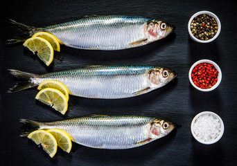 Fresh raw herrings with herbs served on black stone on wooden table 