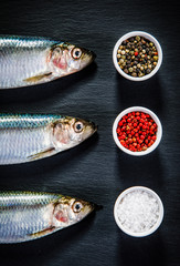 Fresh raw herrings with herbs served on black stone on wooden table 