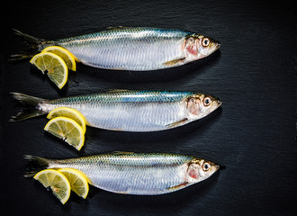 Fresh raw herrings served on black stone on wooden table 