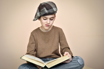 Young boy with cap sitting, holding an old book on the lap and reading. Vintage style.