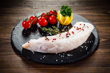 Fresh raw cod with herbs served on black stone on wooden table
