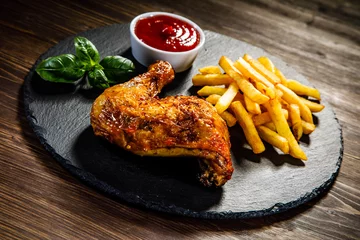 Poster Grilled chicken leg with French fries served on black stone on wooden table © Jacek Chabraszewski