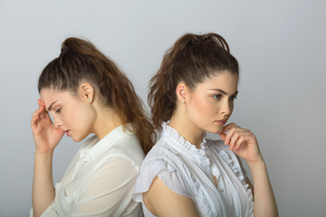 two beautiful sisters twin girls with a severe facial expression in white blouses on a light background