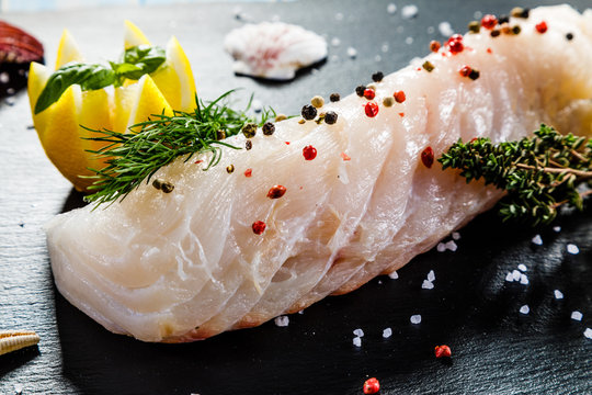 Fresh raw cod with herbs served on black stone on wooden table