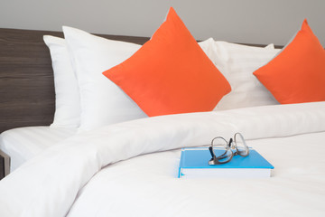 modern glasses on blue book cover with white bed in bedroom.