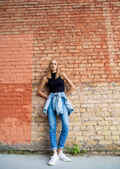 Fototapeta na wymiar fashion girl standing near brick wall in denim and sneakers. Vogue Style