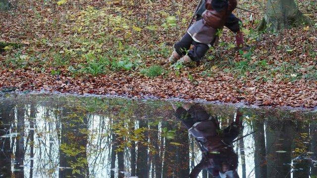 Two warriors Viking are fighting with swords in the forest reflected in water.