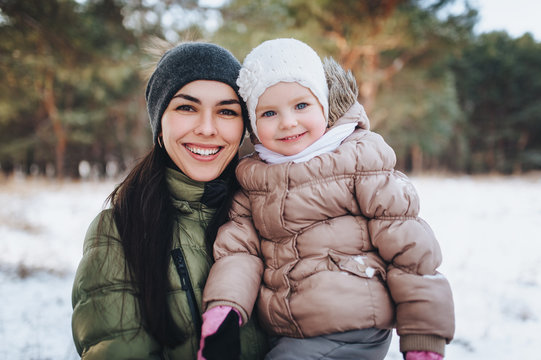 A beautiful young mother is holding a lovely little daughter in her arms and smiling. Winter forest, Christmas vacation.