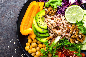 Buddha bowl dish with brown rice, avocado, pepper, tomato, cucumber, red cabbage, chickpea, fresh lettuce salad and walnuts. Healthy vegetarian eating, super food. Top view