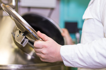Person wearing white lab coat opening a tank, beer ptoduction site