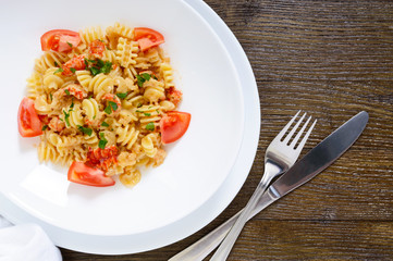 Warm salad with seafood in a white bowl on a wooden background. Pasta Radiatori with crayfish, shrimp, tomatoes, herbs and creamy garlic sauce.