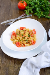 Warm salad with seafood in a white bowl on a wooden background. Pasta Radiatori with crayfish, shrimp, tomatoes, herbs and creamy garlic sauce.