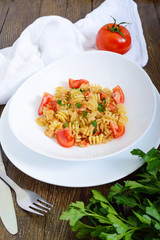 Warm salad with seafood in a white bowl on a wooden background. Pasta Radiatori with crayfish, shrimp, tomatoes, herbs and creamy garlic sauce.