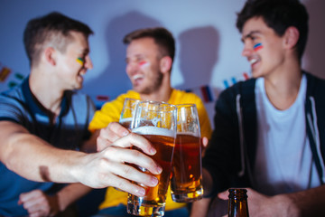 Soccer or football fans watching the match at home, cheering and celebrating goal and drinking beer. Focus on glasses