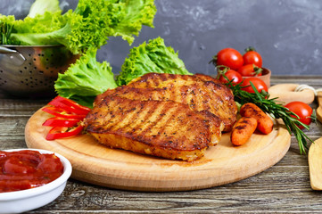 Juicy steaks with greens and vegetables on a wooden tray. A large piece of pork tenderloin grilled.