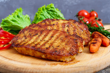 Juicy steaks with greens and vegetables on a wooden tray. A large piece of pork tenderloin grilled.