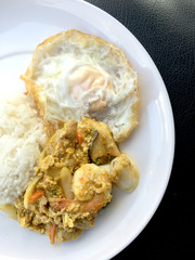 Stir fry prawns and squid with curry power thai style with fried egg with rice in white dish on black fabric texture background. Thai style food.