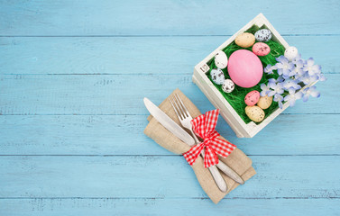 Fork and knife at napkin,easter nest with eggs  on blue wooden board.Easter table set with space for text