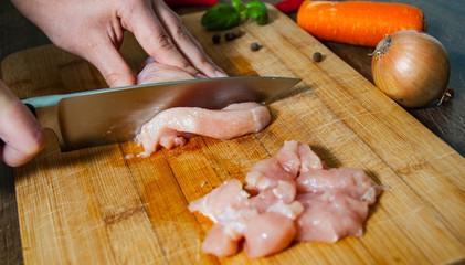 Cook chef hands woman cuts raw chicken breast on a wooden background.