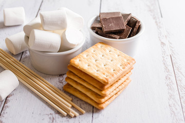 Smores dessert ingredients on wooden table. Picnic or camp concept. Homemade S'more with chocolate and marshmallow on cracker.