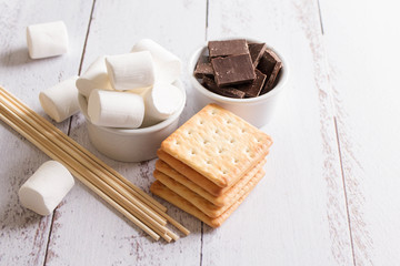 Smores dessert ingredients on wooden table. Picnic or camp concept. Homemade S'more with chocolate and marshmallow on cracker.