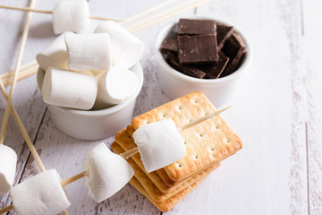 Smores dessert ingredients on wooden table. Picnic or camp concept. Homemade S'more with chocolate and marshmallow on cracker.