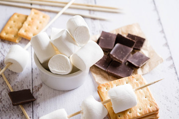 Smores dessert ingredients on wooden table. Picnic or camp concept. Homemade S'more with chocolate and marshmallow on cracker.