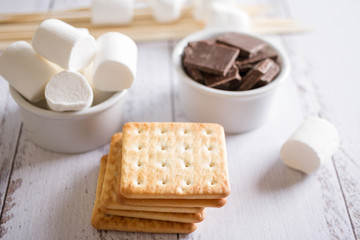 Smores dessert ingredients on wooden table. Picnic or camp concept. Homemade S'more with chocolate and marshmallow on cracker.