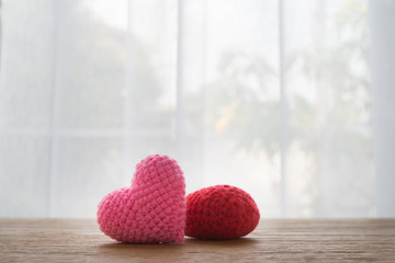 Wood Office table with Beautiful  Couple knitted fabric heart shape  on white curtain windows texture background. view from front office table. concept of valentine's day and heath care.