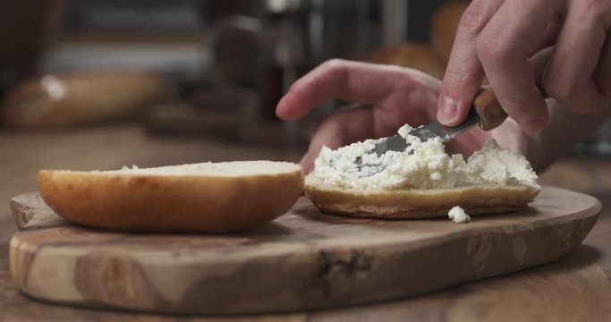 Man hands spreading cream cheese on bagel on wood board