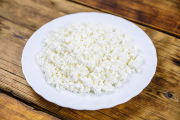 Home made fresh large cottage cheese on white plate on wooden background. Top view.