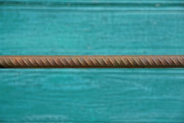 длинный ржавый прут из стали на фоне зелёной стены